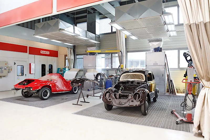 A dedicated paint preparation area shows a red sports car and a classic VW Beetle shell being restored.