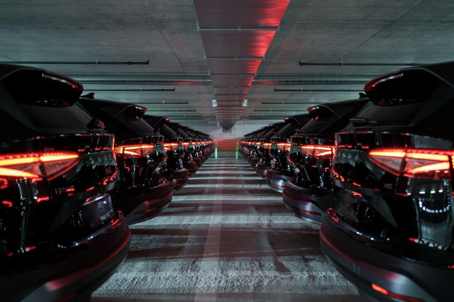 A dramatic underground parking hall lined with rows of identical dark cars with glowing red taillights — visually striking image conveying scale and automotive passion.