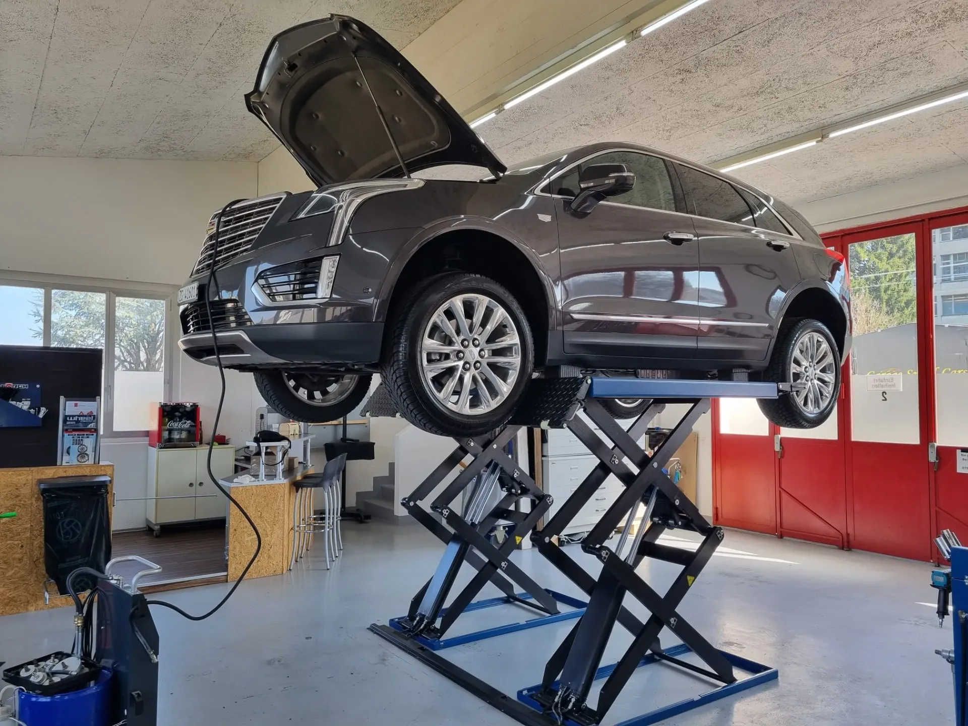 A dark grey Cadillac SUV raised on a scissor lift inside a clean, well-lit workshop.