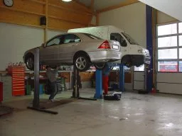A silver car raised on a hydraulic lift inside a professional garage workshop.