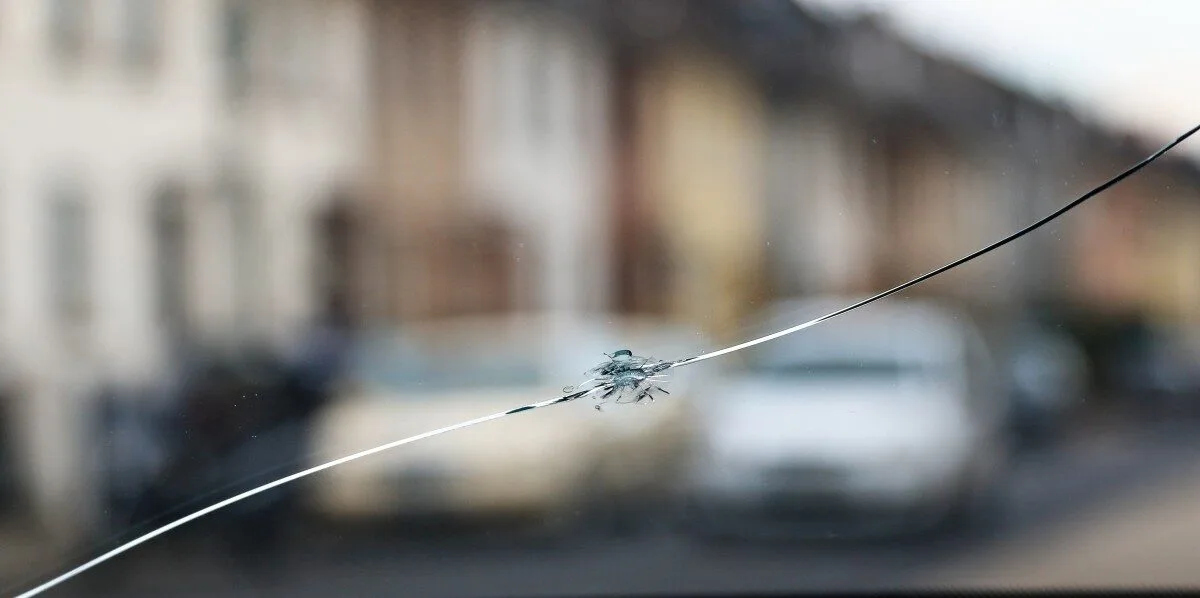Close-up of a cracked windscreen with a stone chip impact point and spreading fracture line.