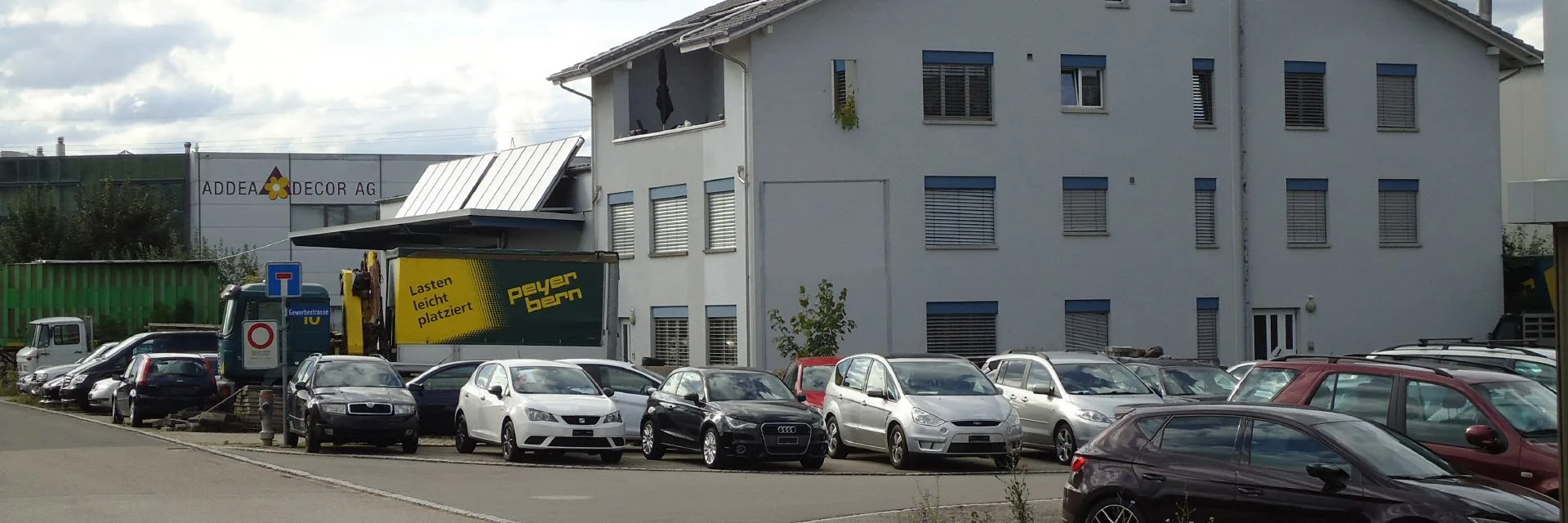 Wide exterior view of the M+C Design garage building with parked cars in the forecourt.