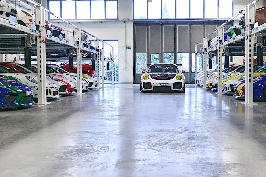 A dedicated storage hall displays rows of colorful Porsche race cars on multi-level stacking systems.