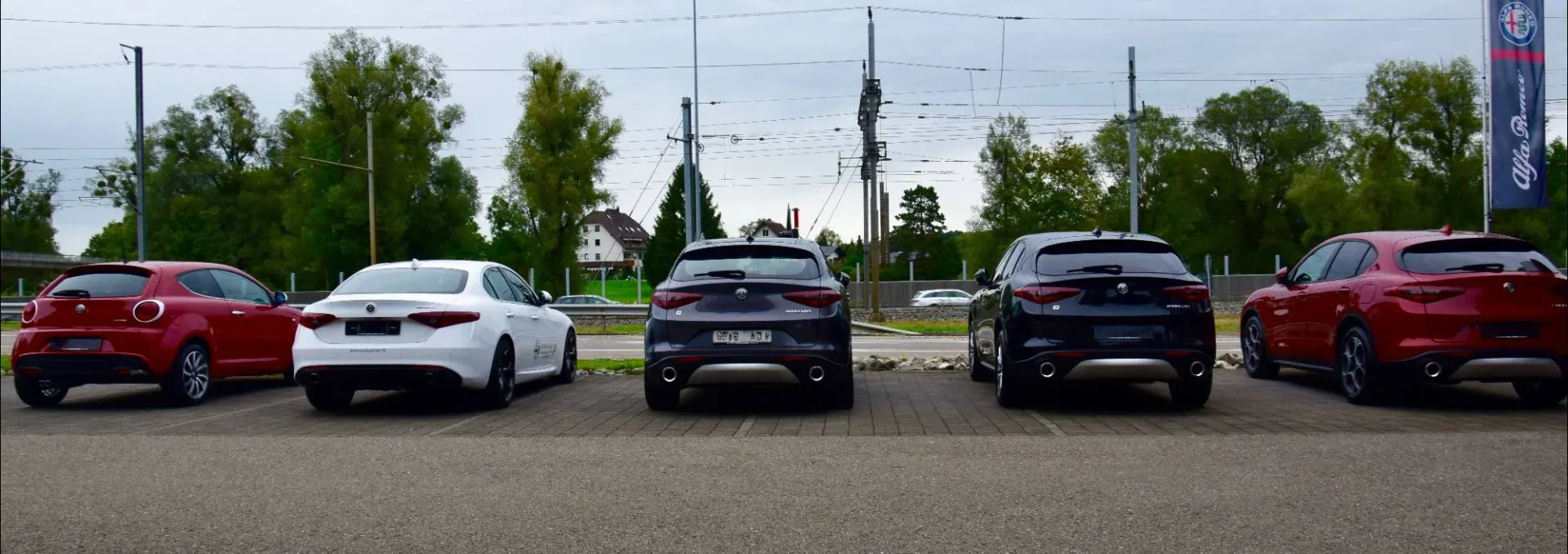 Five Alfa Romeo models parked rear-facing in a dealership lot showcasing the full lineup.