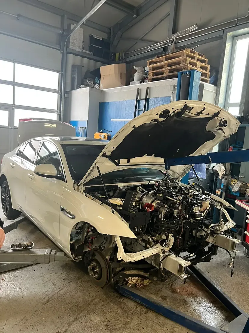 A heavily disassembled white sedan on a lift with the engine exposed during major repair work.