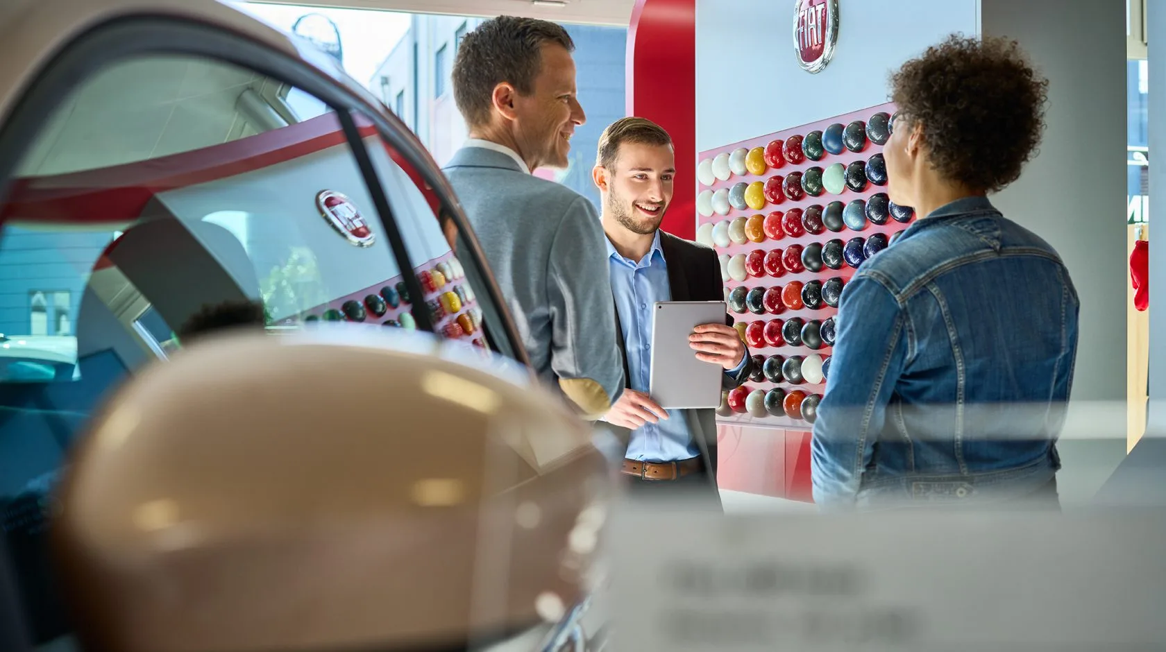 A Fiat showroom consultant engages warmly with two customers, perfectly embodying Garage Bosshardt's philosophy of personal, relationship-driven car buying.