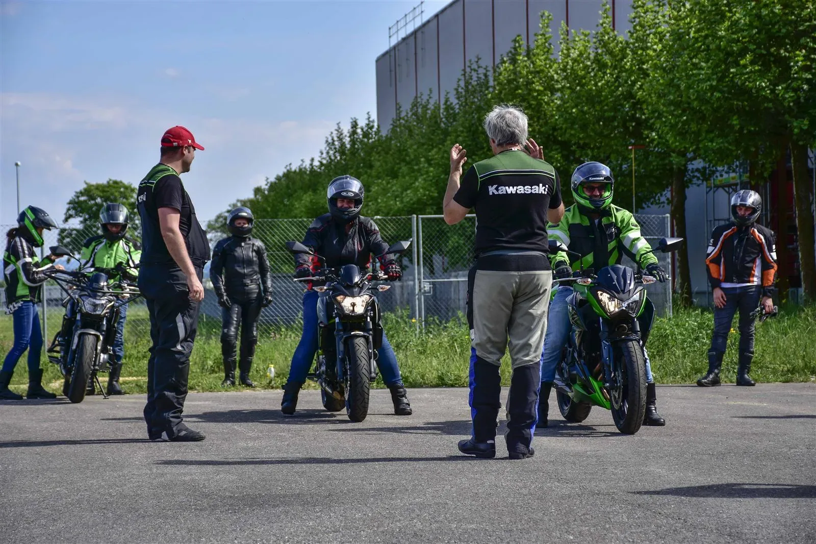 An instructor in a Kawasaki shirt coaches riders during an outdoor motorcycle training session.