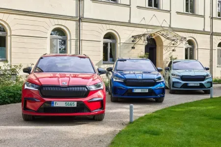 Three Škoda Enyaq electric SUVs in red, blue, and silver parked before an elegant building — showcases the modern, diverse Škoda lineup available at Autocenter Senn.
