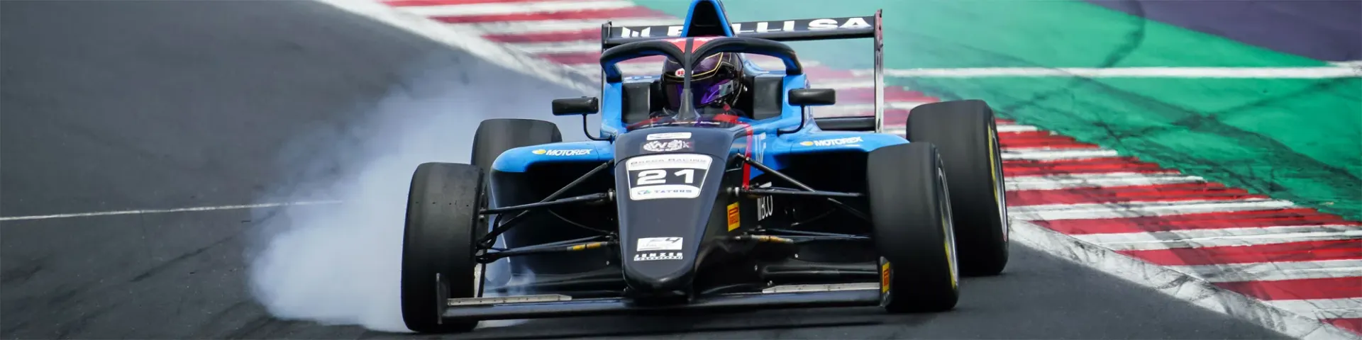 A blue and black Formula 4 car number 21 cornering with tire smoke on a racing circuit.