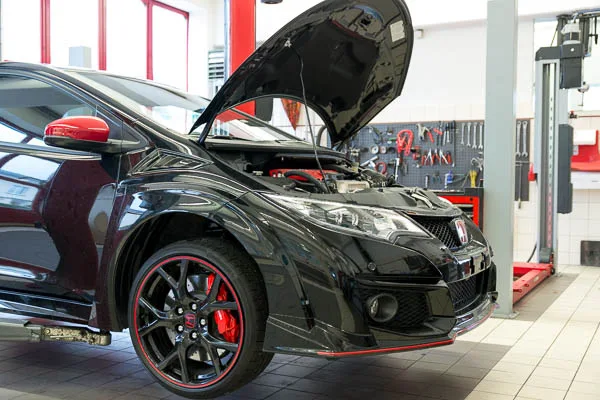Black Honda Civic Type R with hood open being serviced inside a professional workshop.