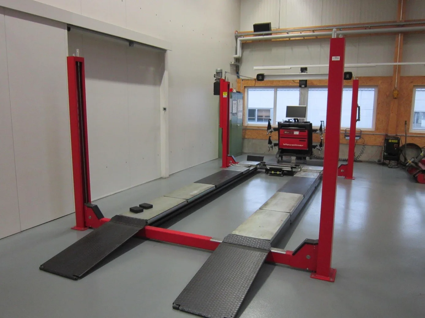 Four-post alignment lift showing ramp entry platforms and wheel-alignment measurement equipment in workshop.