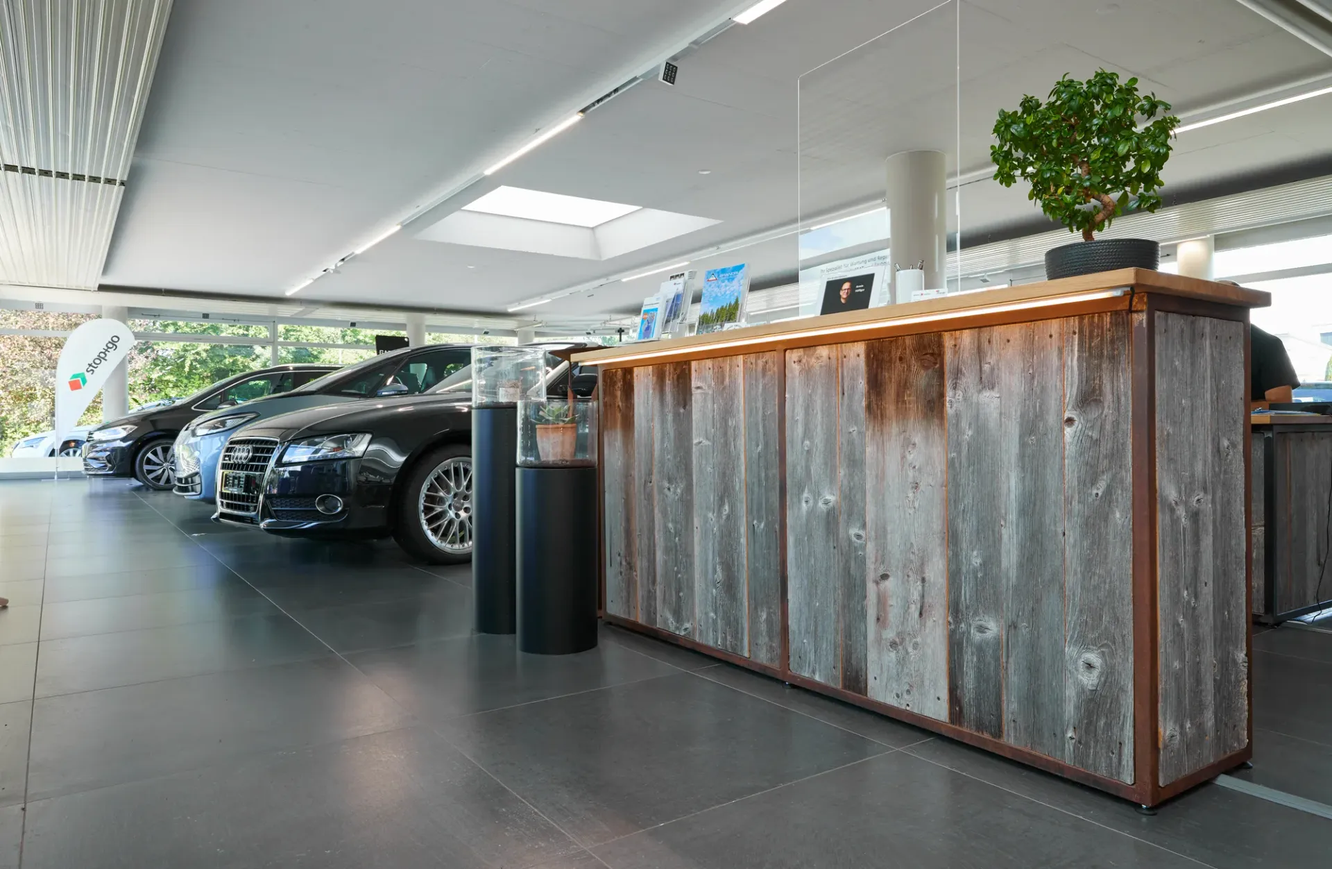 Bright dealership showroom with Audi and other vehicles beside a rustic wooden reception counter.