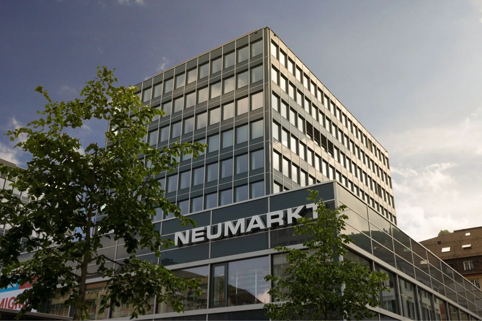 Modern Neumarkt building exterior with glass facade and signage under a blue sky.